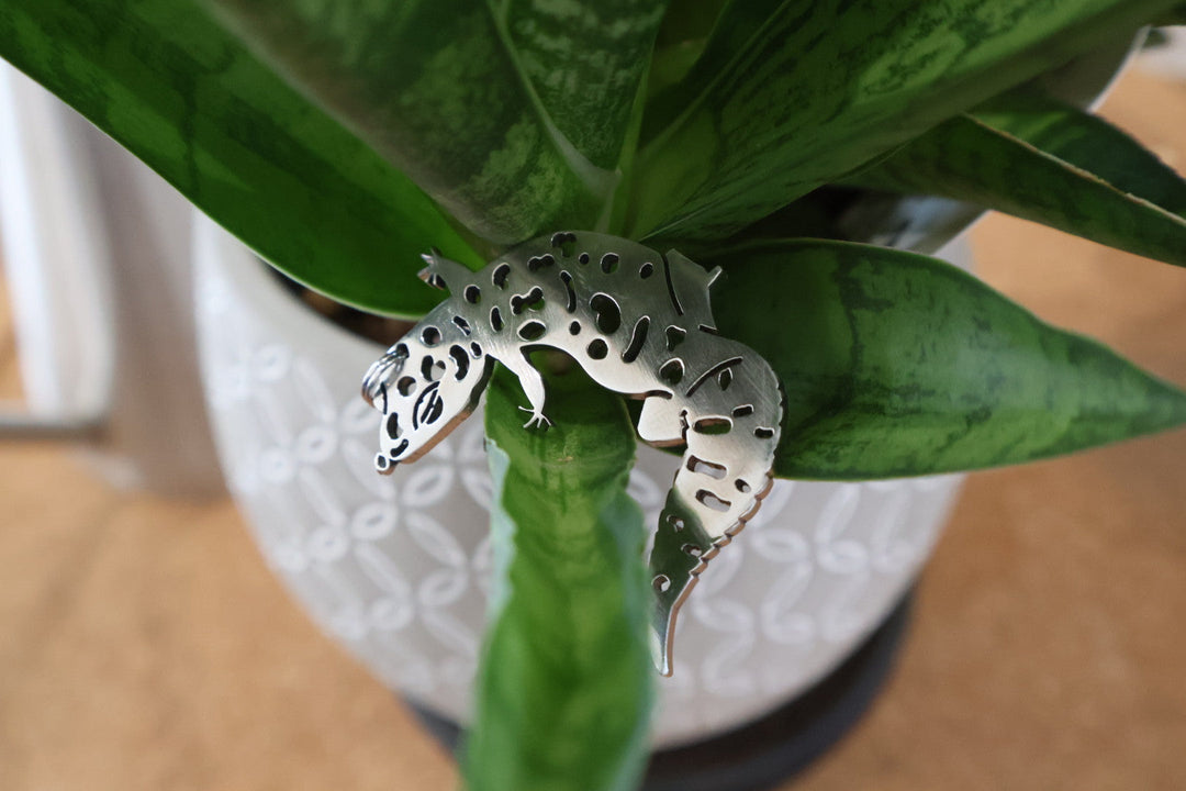 観葉植物の葉の上に置かれた、斑点模様のある銀色のトカゲ形アクセサリー